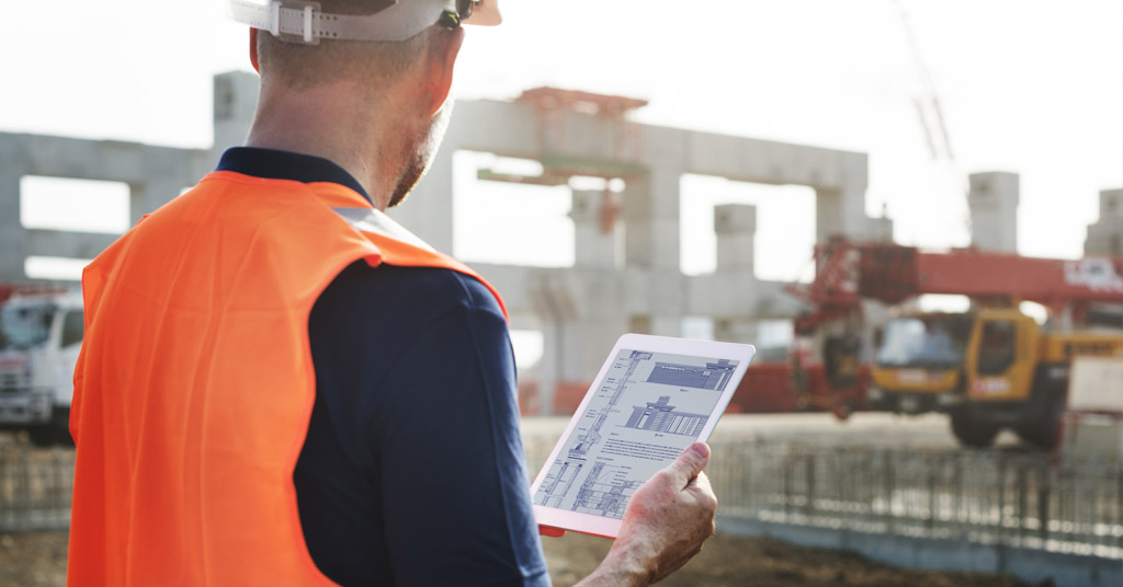 man holding tablet while looking at construction site.