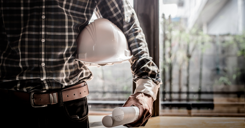 Man holding a construction hat in his arm with blueprints in his hand.