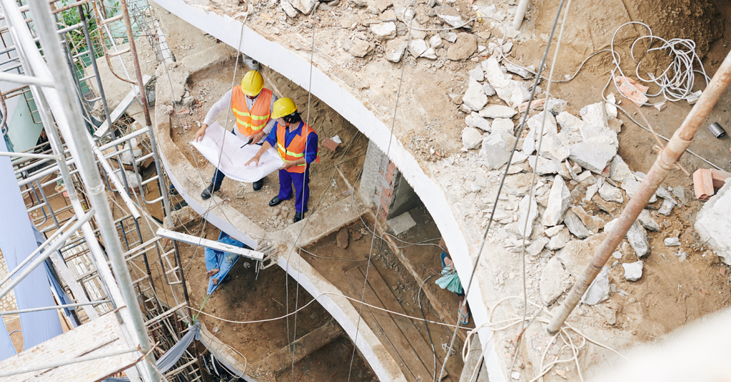 construction workers looking over blue prints in broken building structure.