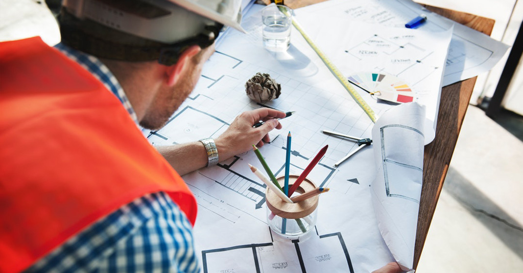 Male construction worker writing on blueprints on desk.