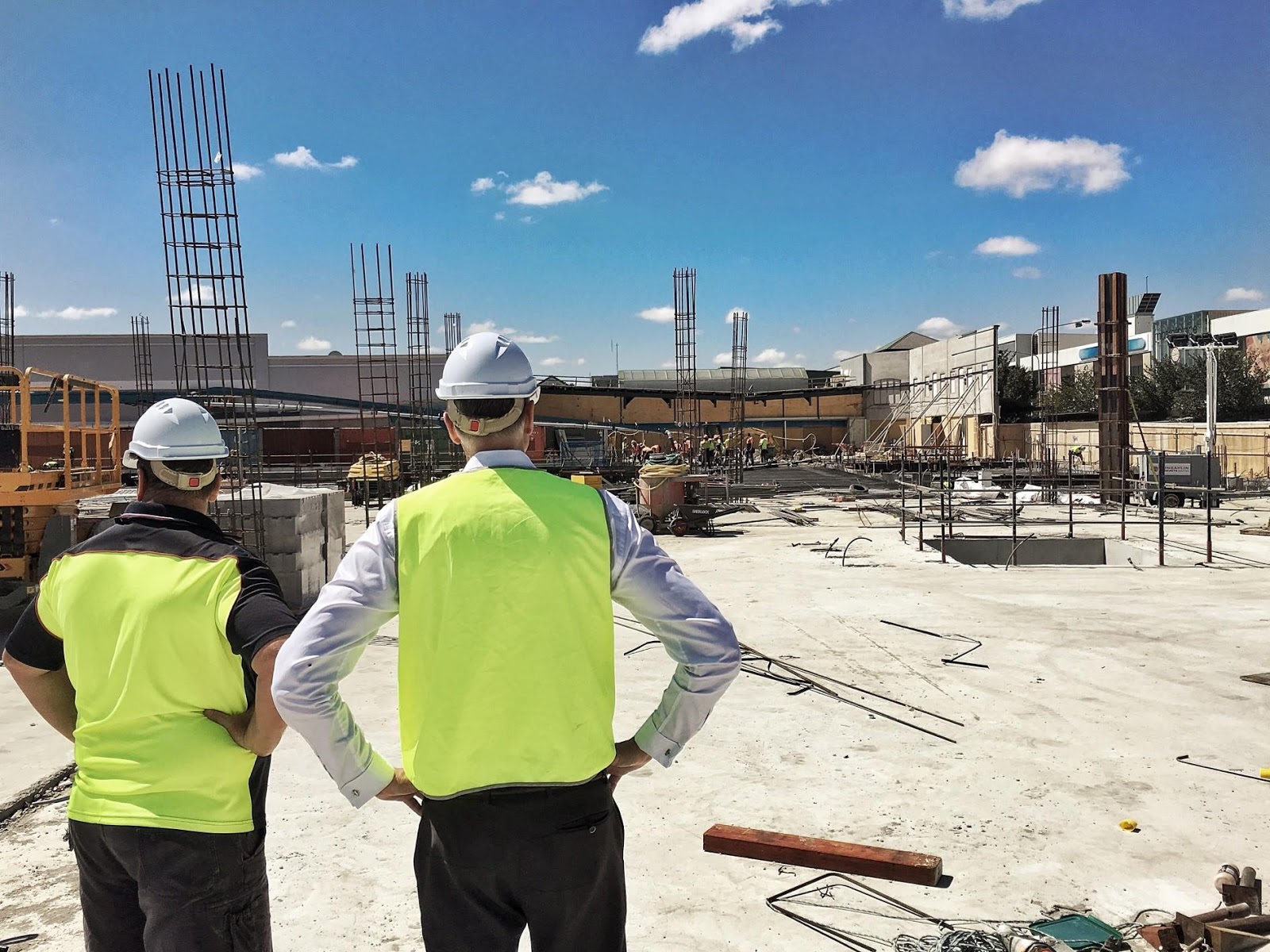 Two male construction workers standing while looking at unfinished building.