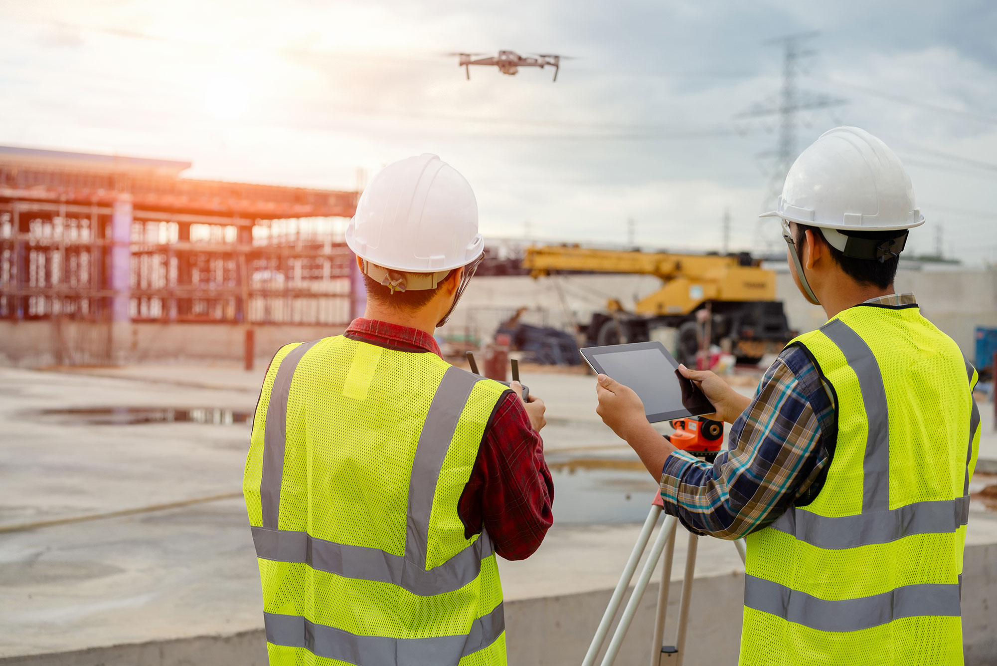 two construction workers looking at a building while one holds a tablet.