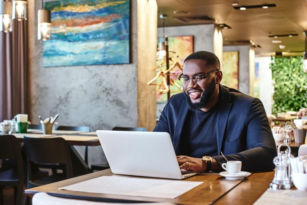African American man working on his laptop at a fancy restaurant drinking coffee.