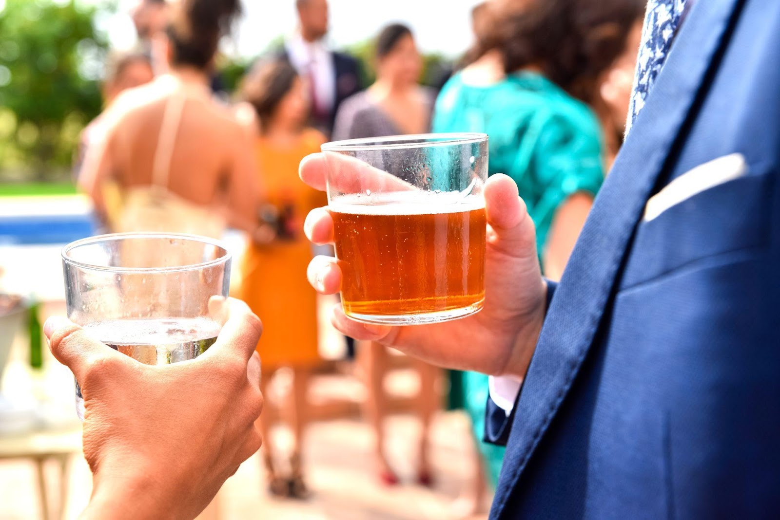 People talking and holding drinks at an outside event.