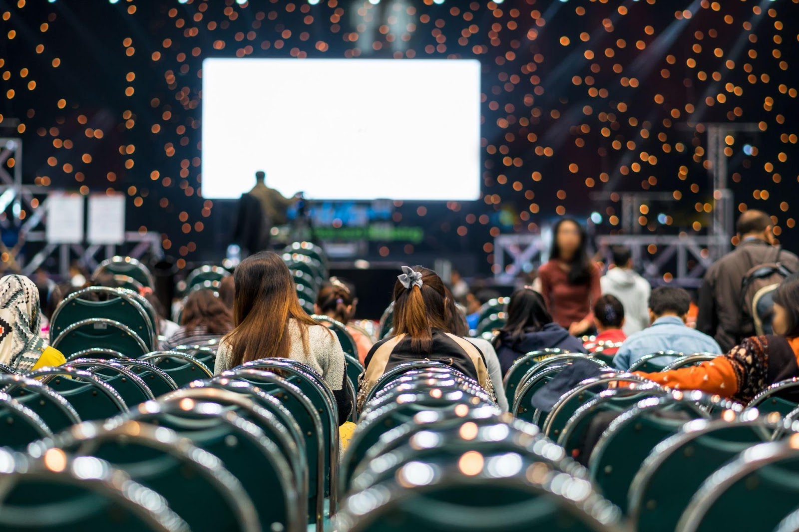 People sitting in green chairs while in front of a stage.