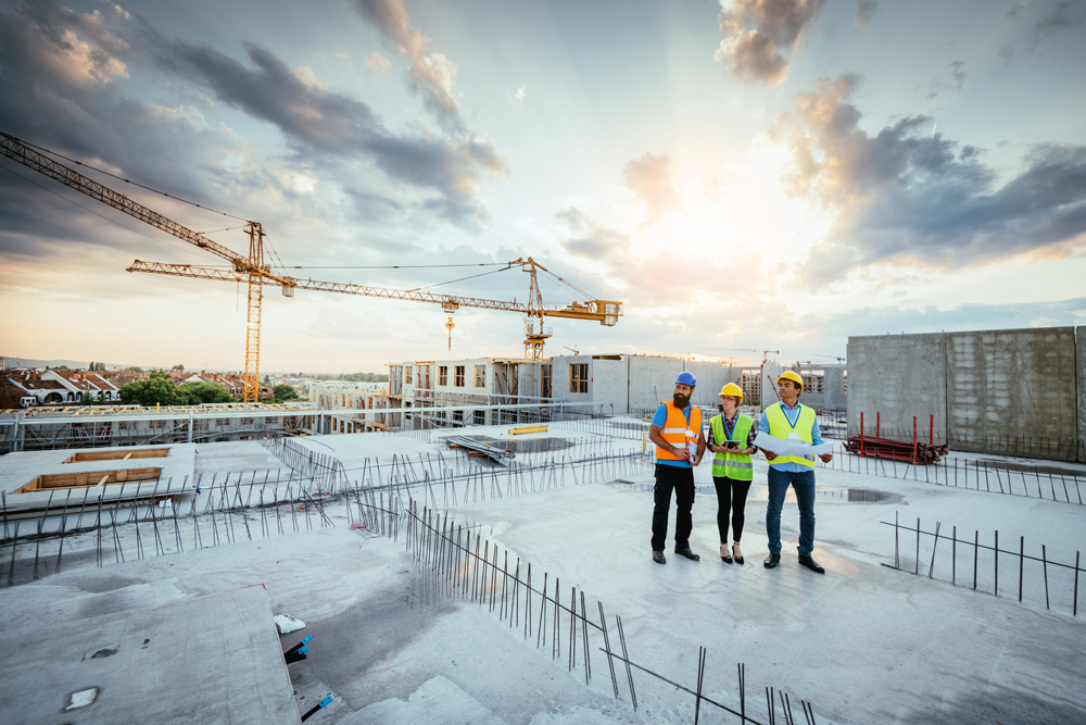 three construction workers on top of unfinished building looking out in the distance.