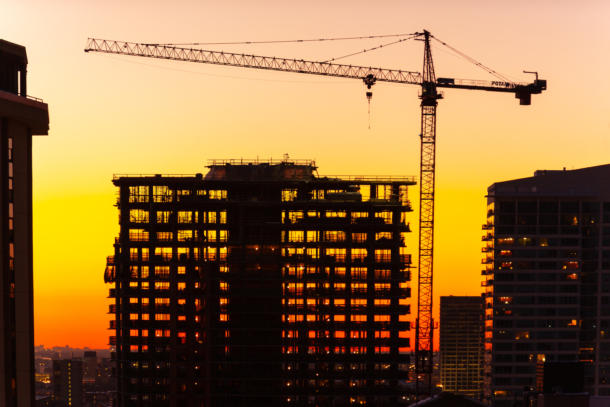 Silhouette Of Crane And Building Under Construction At Dusk.