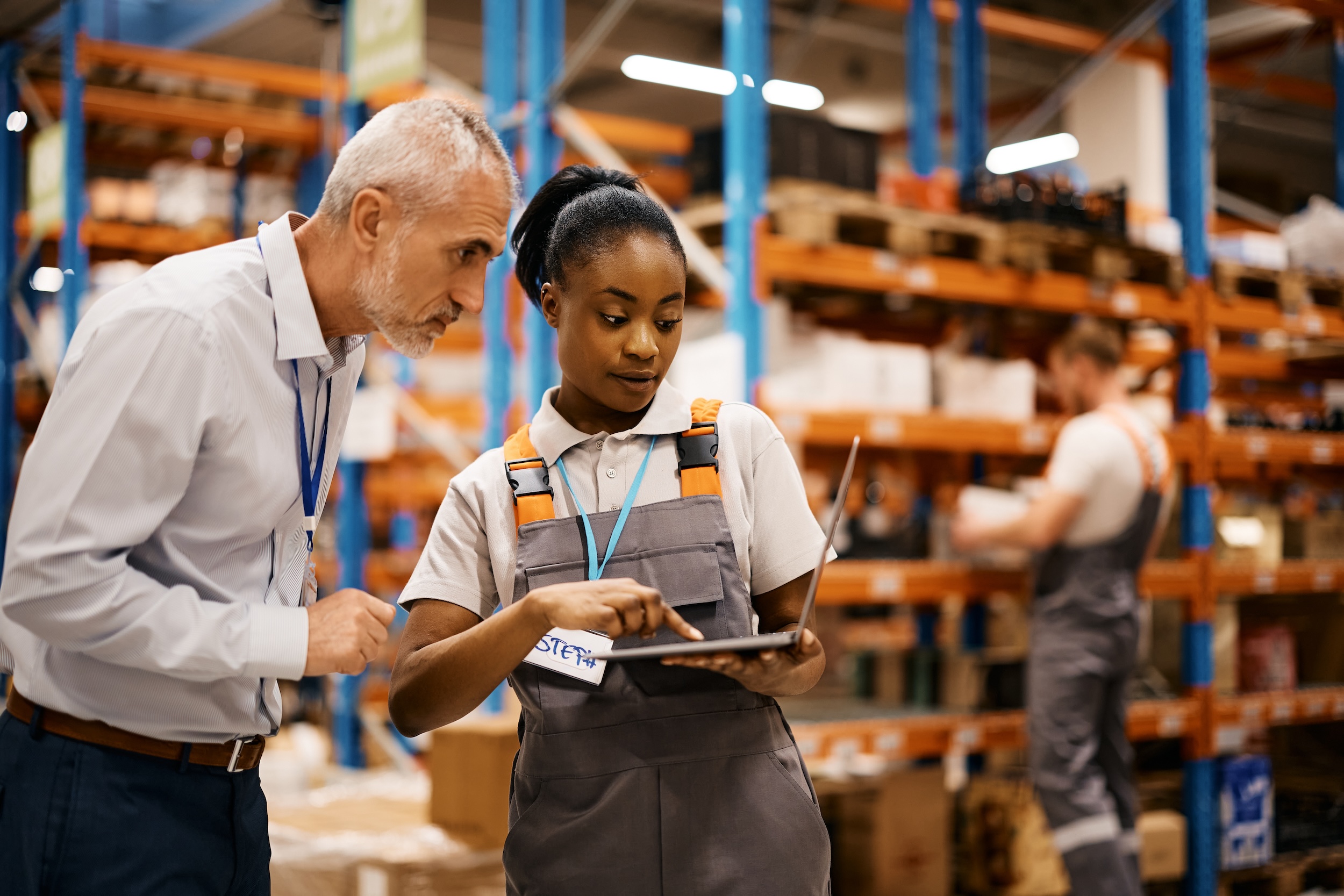 Black Distribution Warehouse Worker And Her Manager Using Laptop At Storage Compartment.