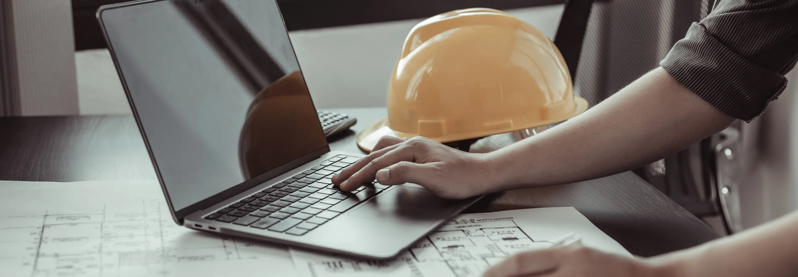 Young Man With A Laptop Plotting A System Of Building Structures In Blueprints, Architects Or Engineers Are Designing Buildings Using Computers To Calculate The Physical Structure To Be Correct.